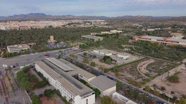 Drone footage flying over IES Misteri d'Elx school in Elche, Spain, early morning. Torre del Vaillo visible in the background against a scenic sky.