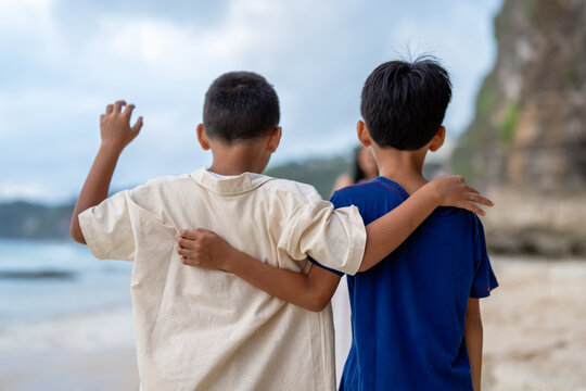 Back view of two young brothers standing together with arms around shoulders at beach
