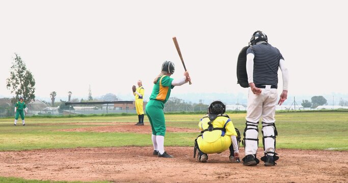 Diverse softball players and umpire waiting on community field holding bat, glove, mask