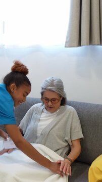 Attentive latina caregiver covering a senior woman with a warm blanket on the couch during a home healthcare visit