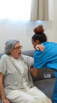 Compassionate latina caregiver assisting an elderly patient in standing up from the couch, supporting her mobility during home rehabilitation