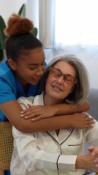 Compassionate latina home health nurse hugging and comforting smiling senior patient while visiting indoors