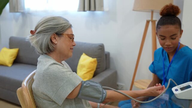 Caring latina nurse checking the blood pressure of a senior woman with an automatic tonometer during a home care checkup
