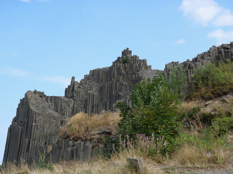 Basalt columns of Panska Skala form a striking rock formation. The side view shows layered columns among natural vegetation.