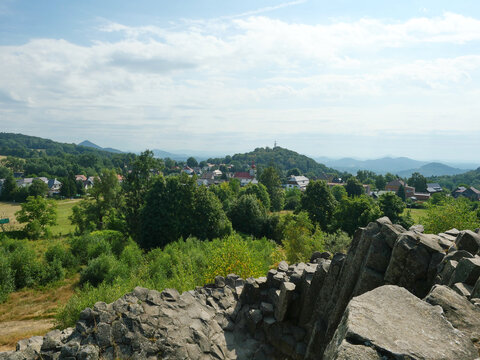 View from Panska skala across a village and forested hills toward the hazy horizon. Basalt rock frames the foreground.