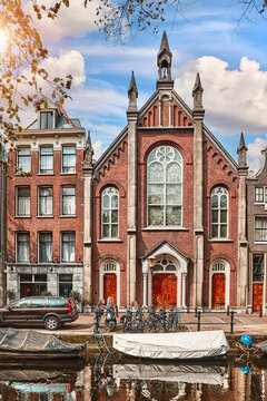 Amsterdam, Netherlands. Vintage brick church and historic buildings stand by a canal waterfront. Classic European architecture with a traditional boat and bicycles captures a scenic retro city vibe.