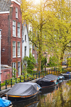 Amsterdam, Netherlands. Vintage brick canal houses stand along the waterfront with traditional boats. Classic European architecture and autumn trees capture a scenic retro city vibe.