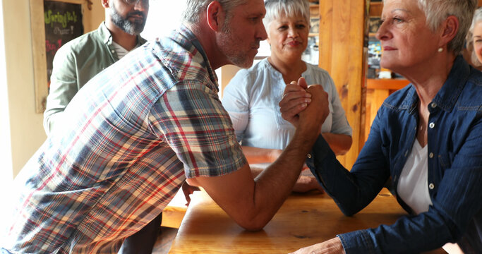 Spectators watch two middle-aged people arm wrestle at a table.