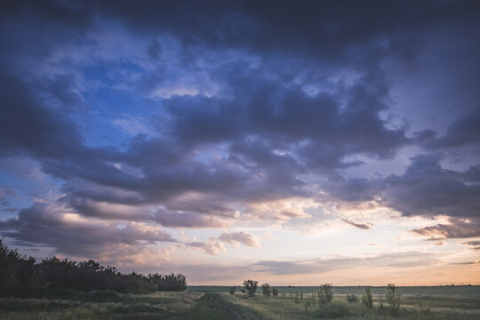 A cloudy evening sky at sunset over the Kazakh steppes, featuring rain clouds and sunbeams&mdash;a summer landscape under overcast skies, with rain visible on the horizon