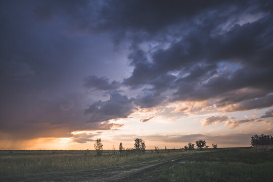 A cloudy evening sky at sunset over the Kazakh steppes, featuring rain clouds and sunbeams&mdash;a summer landscape under overcast skies, with rain visible on the horizon