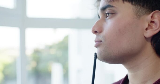 African American man in maroon sweater holding pen over open notebook while looking through window