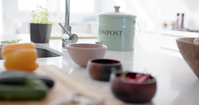 Kitchen counter holding compost caddy, vegetables while focus shifting over cutting board and bowls