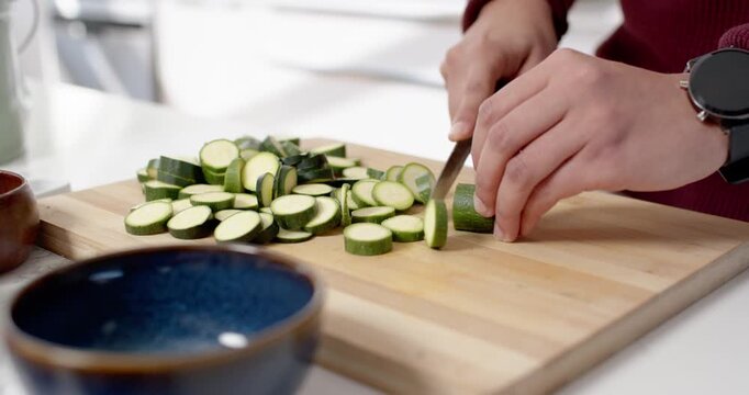 Hands slicing zucchini on wooden cutting board while knife chopping rounds into growing pile