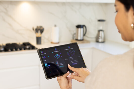 Woman standing in white kitchen holding tablet displaying dashboard interface with bar chart