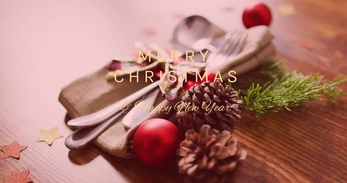 Folded napkin holding silver cutlery beside red ornaments, pinecones on wooden tabletop, copy space