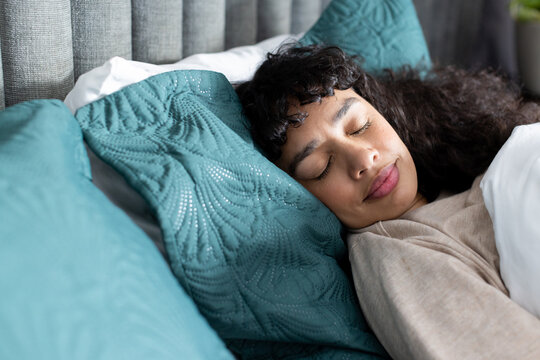 African American woman with dark curly hair sleeping on teal quilted pillow in bed