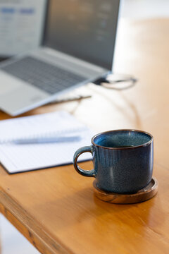 Dark blue speckled mug resting on wooden coaster near notebook and pen on desk, copy space