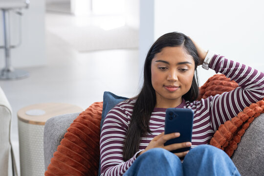 African American woman sitting on gray couch holding dark smartphone while looking at screen