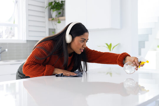 African American woman in sweater wiping kitchen island with blue cloth and spray bottle