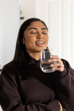 African American woman holding glass of water near mouth while tilting head back with closed eyes