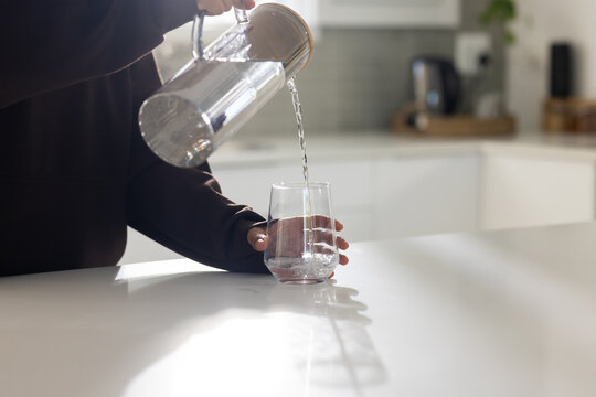 African American person's hands pouring water from clear pitcher into glass on white countertop