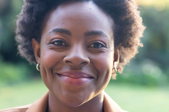 African American woman with curly hair facing camera wearing tan top and gold hoop earrings