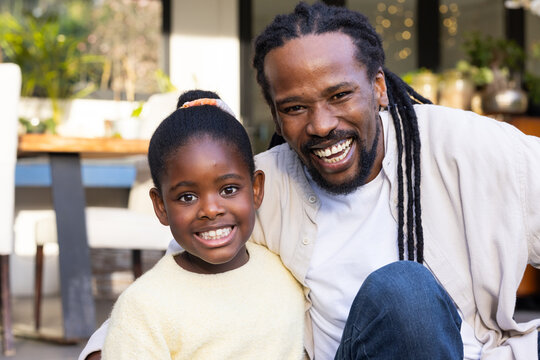 African American dad and daughter posing closely together in outdoor patio area with potted plants
