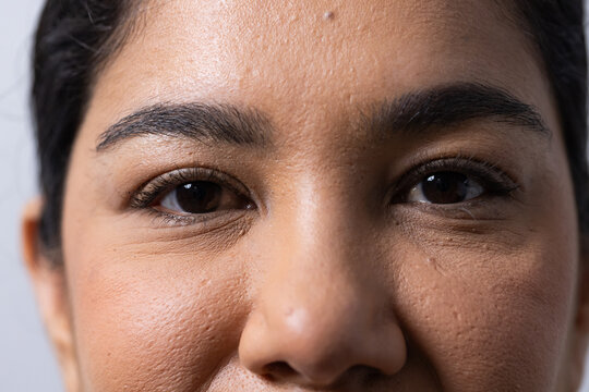 Woman looking forward with dark eyebrows and brown eyes filling tight frame against plain backdrop
