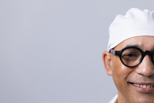 African American man wearing white head covering and black round glasses standing at gray backdrop
