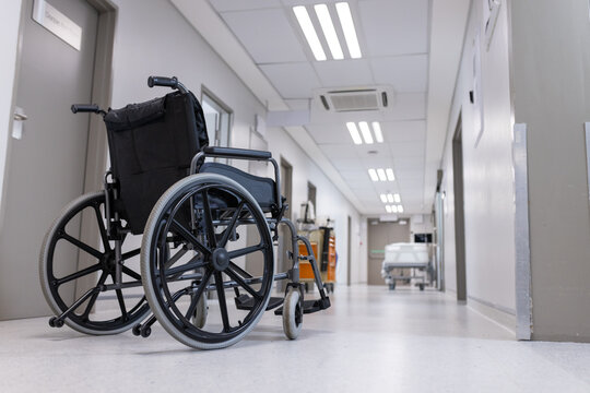Empty black manual wheelchair resting in hospital corridor with gray doors and ceiling lights