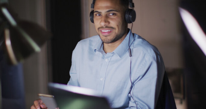 Image portrait of smiling businessman wearing headphones, working at night in office