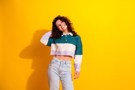 Smiling young woman in crop polo and jeans posing against a bright yellow background, casual fashion portrait conveying joy, confidence and playful summer style