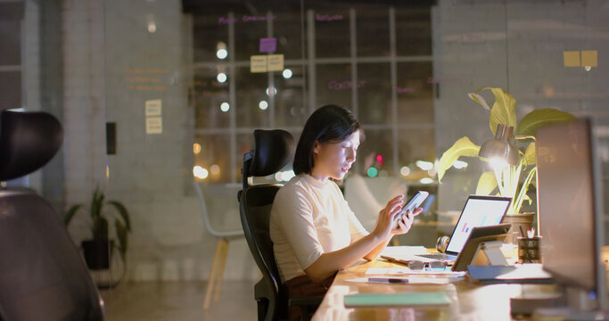 Asian casual businesswoman using smartphone, laptop and tablet in office at night