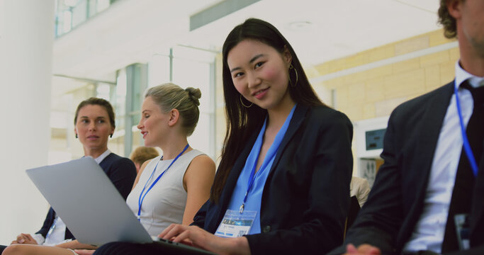Happy asian businesswoman sitting with laptop among audience at business conference