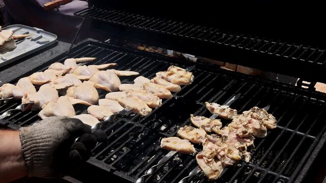 Raw chicken wings with marinated meat skewers placed on charcoal grill being adjusted for cooking