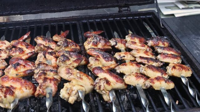 Several chicken wing skewers grilling on barbecue, showing cooking progress