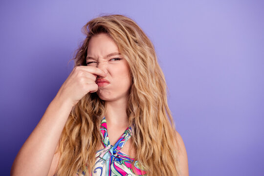 Young woman holding her nose in disgust at a bad smell, portrait of blonde with long hair against a purple background