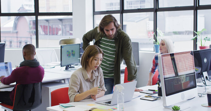 Diverse business people using laptops going through paperwork in modern office