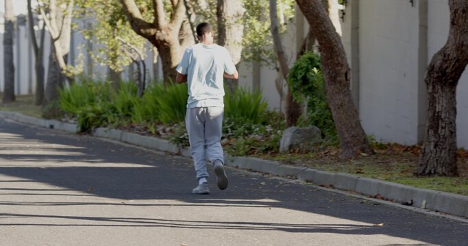 Jogging man wearing light tee gray sweats and athletic shoes moving down residential road by wall