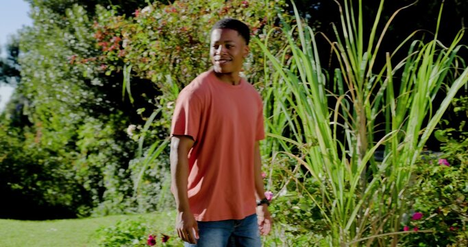 Standing adult male wearing coral T-shirt and jeans in garden, showing wristwatch near tall grasses