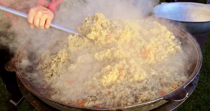 Steaming yellow rice with vegetables being stirred in large outdoor pan over heat