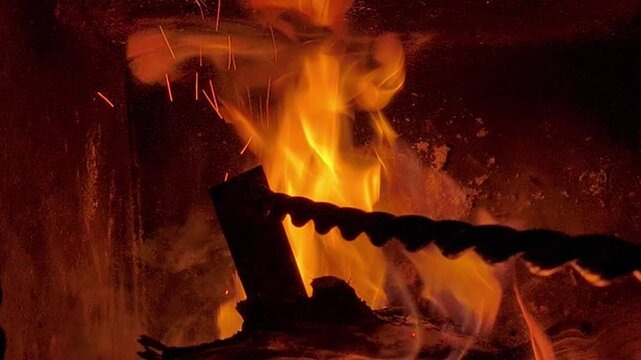 Intense fire burning stacked logs in fireplace, bright flame and glowing blaze forming cozy warm mood indoors, closeup view of natural fire pattern on dark background for lifestyle heating concept