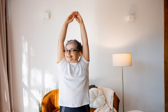 Senior woman stretching overhead at home for healthy aging and daily wellness
