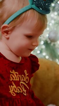Adorable Child in Festive Red Outfit with Holiday Headband Engaged in Playful Activity Surrounded by Twinkling Lights and a Cheerful Atmosphere