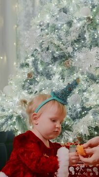 A joyful child in festive attire celebrates the holiday season, wearing a whimsical party hat while surrounded by a beautifully decorated Christmas tree and lights.