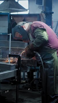 Intense Welding Process Captured: A Skilled Welder Creating Sparks and Melting Metal in a Busy Workshop with Protective Gear and Bright Blue Flames