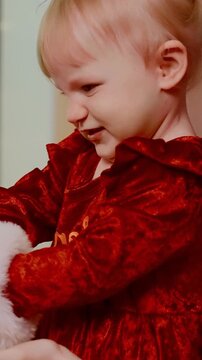 Adorable Toddler Joyfully Engages with Holiday Decorations in Festive Red Outfit, Capturing the Spirit of Christmas Cheer and Childhood Wonder in a Heartwarming Moment