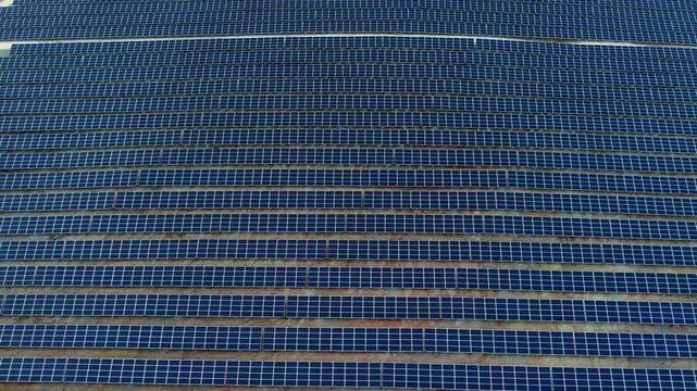Aerial view of an enormous solar farm featuring endless rows of blue photovoltaic panels arranged in precise geometric patterns, showcasing renewable energy infrastructure and clean power generation.
