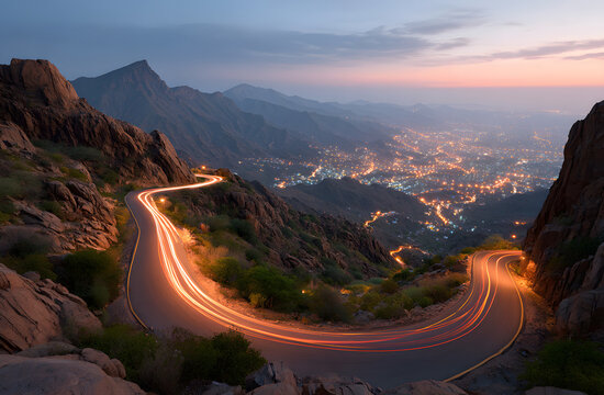 Zigzag mountain road features car light trails at dusk in Al Hada, Taif, Saudi Arabia. Illuminated city lights glow below rocky landscape as vehicles create streaks of light on winding highway,
