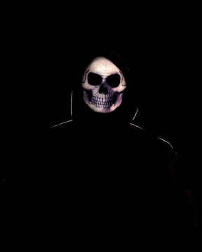 Person wearing a skull mask and black clothes against a black background.